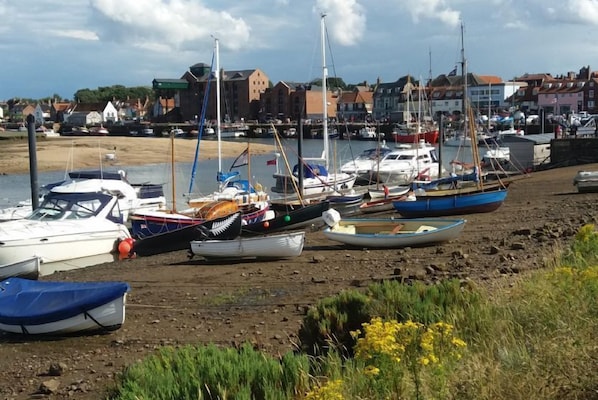 A harbor with various boats docked along the shore, surrounded by buildings and a sandy beach.