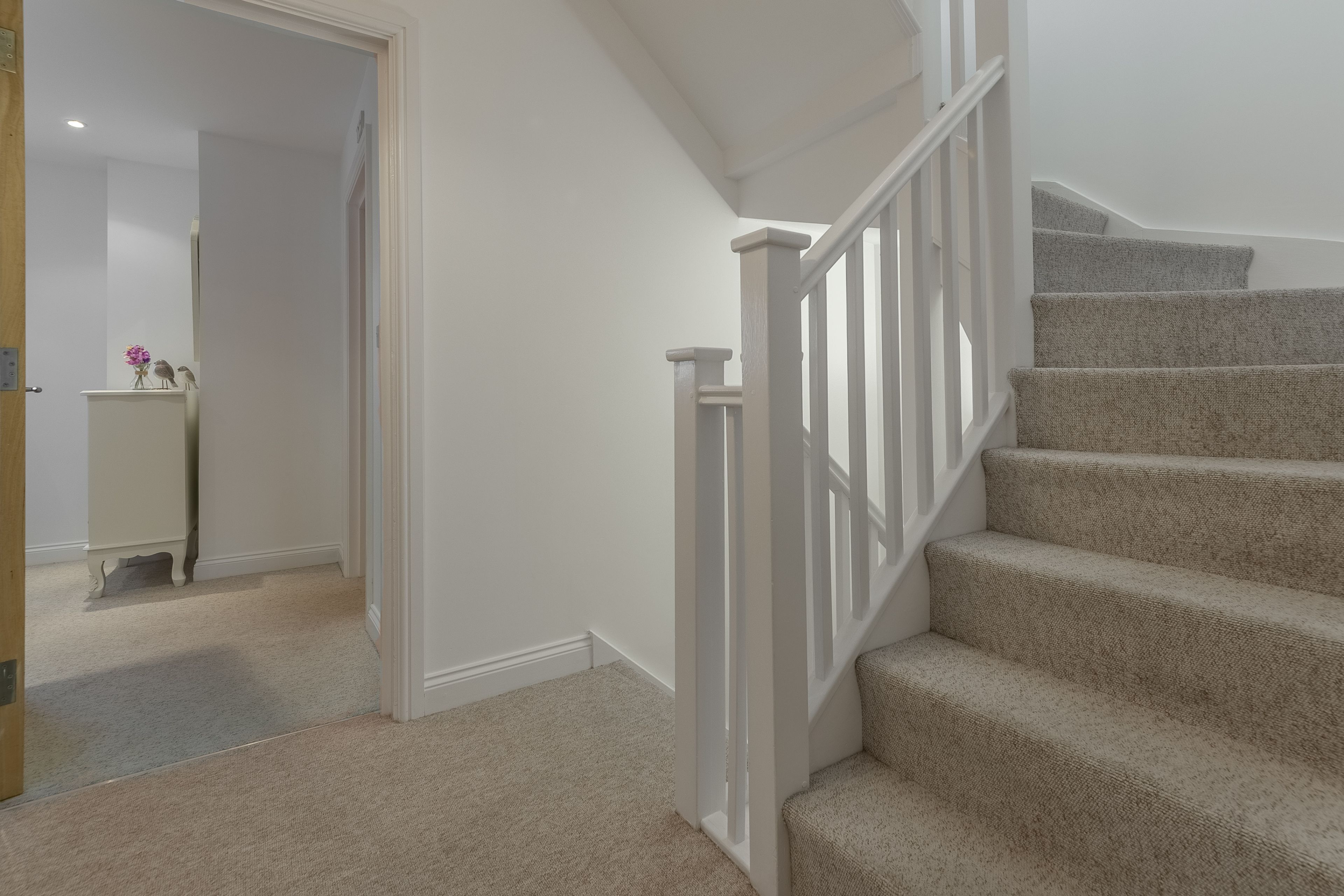 Eine Teppichstufen-Treppe mit weißen Geländern, die zu einer oberen Etage führt.