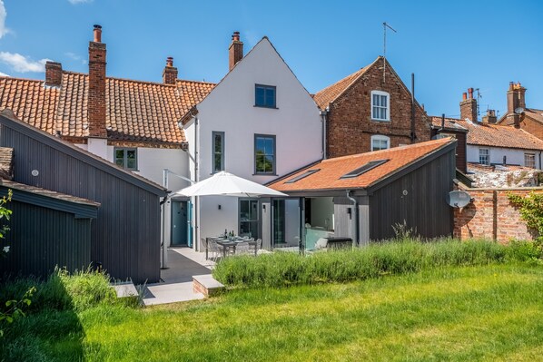 Une maison moderne avec une façade blanche, un toit recouvert de tuiles rouges et un petit patio agrémenté d’une table et de chaises.