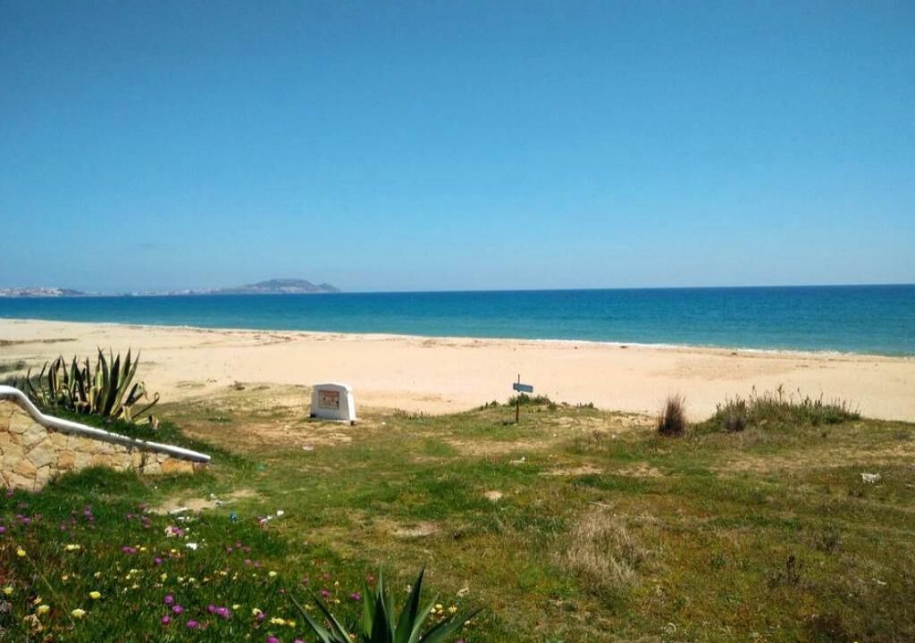 A beach with a clear sky, a white tent, and a signpost in the foreground.