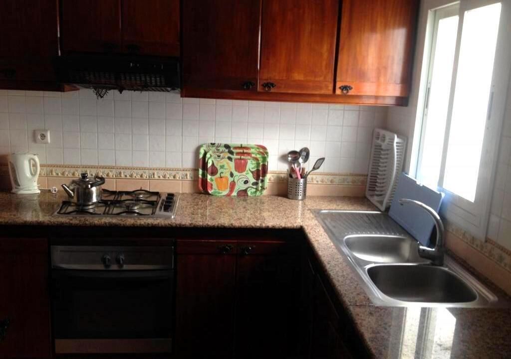 Una cocina con armarios de madera, estufa a gas, lavavajillas y ventana que proporciona luz natural.