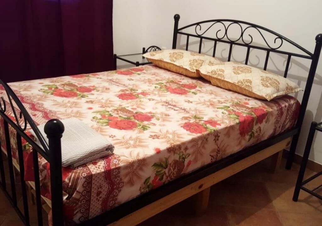 A single bed with a floral bedspread and two pillows, a wooden frame, and a small bedside table.
