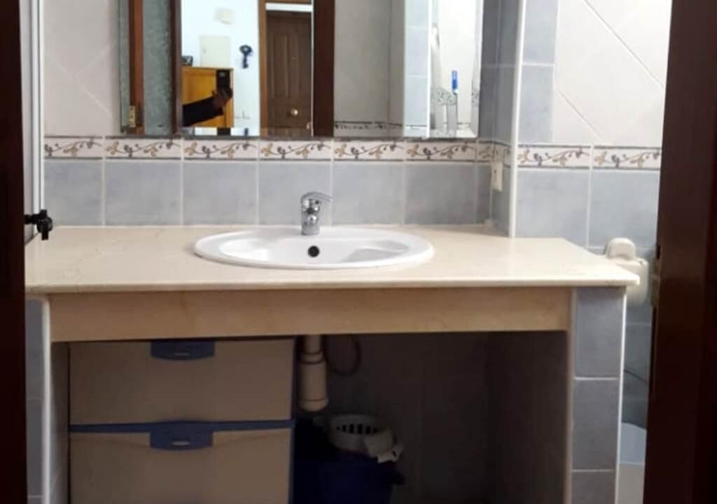 Een badkamer met een wit wastafel, een spiegel erboven en een betegelde spatwand.