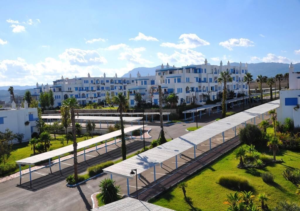 A hotel with a row of white buildings with blue accents, a covered outdoor seating area, and palm trees.