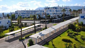 Un hotel con una hilera de edificios blancos con detalles azules, una zona de estar cubierta al aire libre y palmeras.