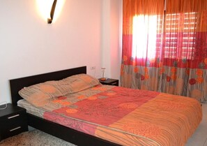 Quarto com cama, mesa de cabeceira e abajur.