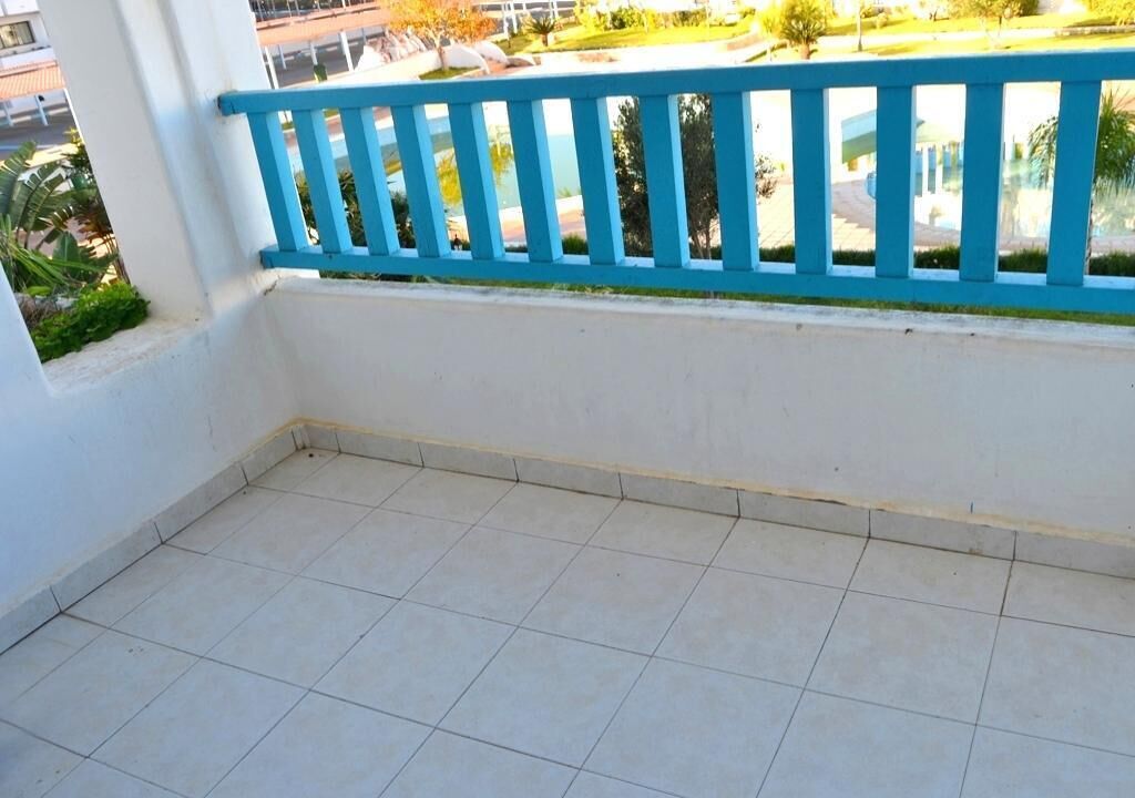 A balcony with a blue railing, white walls, and a tiled floor.