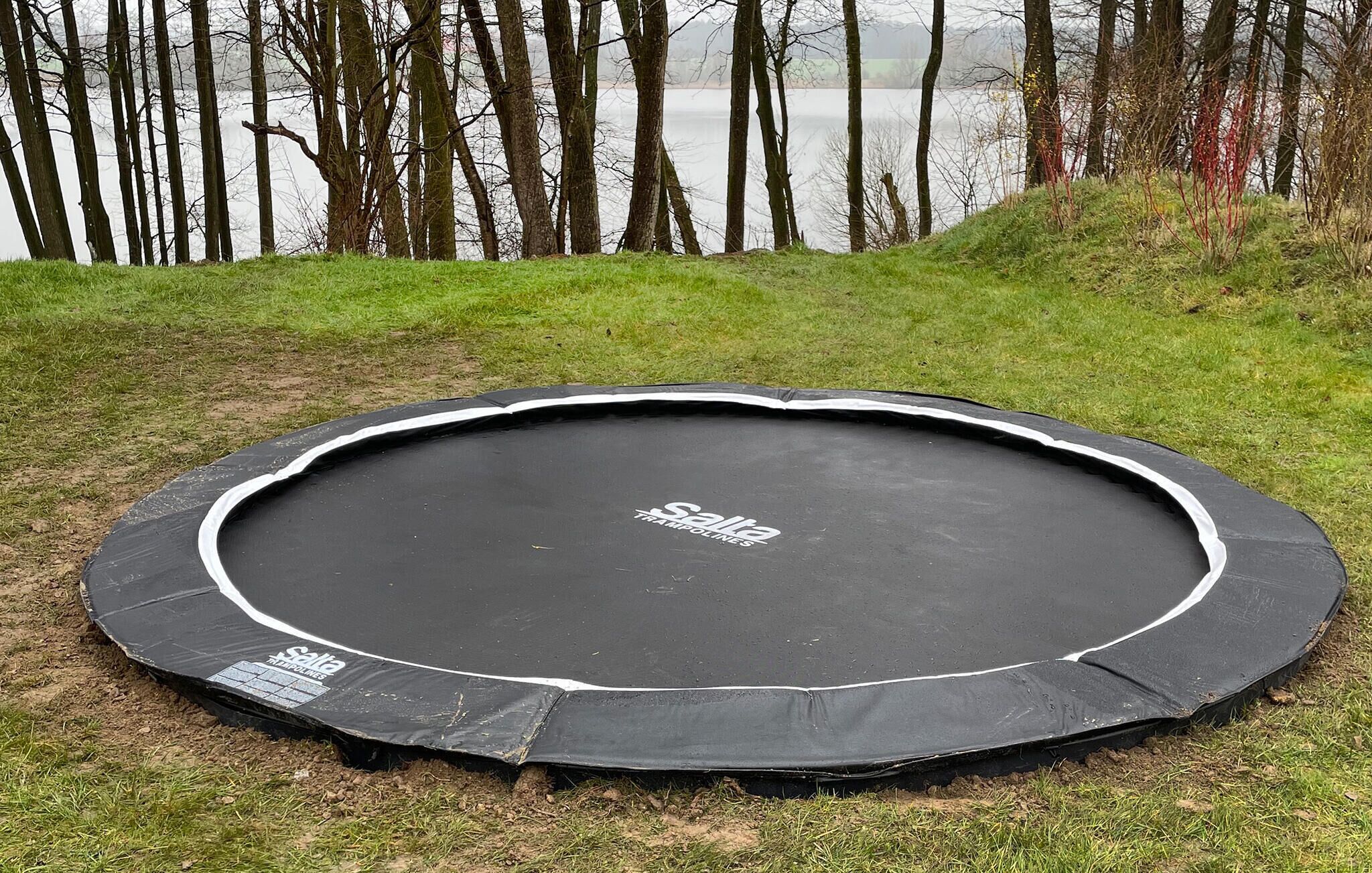 Un trampolín con el nombre de marca 'Salla Trampolines' en su superficie, rodeado de césped y árboles.