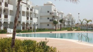 A resort with multiple white buildings, a swimming pool, and palm trees. - The Greens Residence 3649 (Saidia)