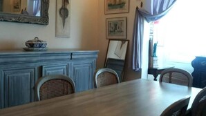 Un coin repas avec une table et des chaises en bois, un miroir décoratif, des œuvres d’art accrochées au mur et une fenêtre avec des rideaux.