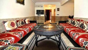 Ein Wohnzimmer mit rundem Couchtisch, zwei Sofas mit gemusterten Kissen, einem Flachbildfernseher und einer Chandelüster.