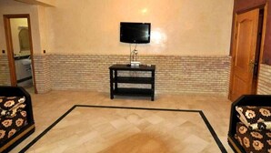 A living room with a flat-screen TV mounted on the wall, a black entertainment unit, and patterned sofas. - Residence Babylone Marrakech 3388 (Marrakech)