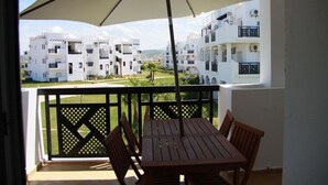 A balcony with a table and chairs, an umbrella, and a view of white apartment buildings.