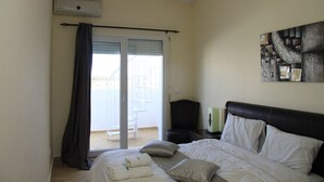 A bedroom with a bed, a nightstand, a lamp, a painting, and a view of the outside.
