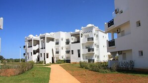 A modern residential building with multiple balconies, a paved walkway, and a well-maintained lawn.