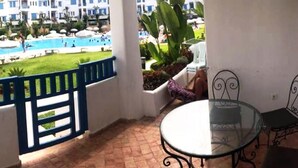 A balcony with a glass table and chairs, overlooking a swimming pool and a building with multiple balconies. - Residence Java Rasmile 2831 (Mdiq)