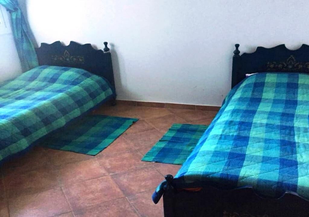 Two twin beds with matching blue and green checkered bedding, a tiled floor, and a plain white wall.