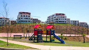 A playground with slides and climbing structures, surrounded by a landscaped area with benches. - Lilac's Garden Residence 2194 (Cabo Negro)