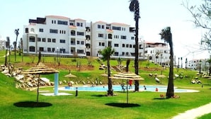 A hotel with multiple white buildings, a swimming pool, and a grassy area with palm trees. - Lilac's Garden Residence 2194 (Cabo Negro)