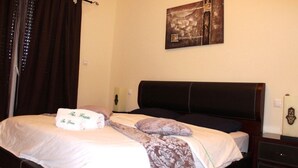 A neatly made bed with a floral-patterned blanket and a white towel with text. - The Greens Residence 2341 (SAIDIA)