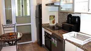 A compact kitchen with a refrigerator, stove, microwave, and a small dining area with a table and chairs. - The Greens Residence 2341 (SAIDIA)
