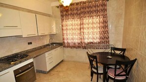 A compact kitchen with a gas stove, oven, and white cabinets. There's a dining table with chairs and a patterned curtain. - ����������������������������������������������������������������������������������������������������������������������������������������������������������������������������������������� (Marrakech)