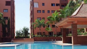 A swimming pool with a tiled deck, surrounded by palm trees and a building with a red facade. - ����������������������������������������������������������������������������������������������������������������������������������������������������������������������������������������� (Marrakech)