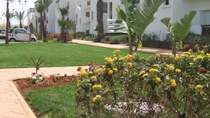 Um edifício residencial com várias varandas, um gramado bem cuidado e uma variedade de plantas floridas.