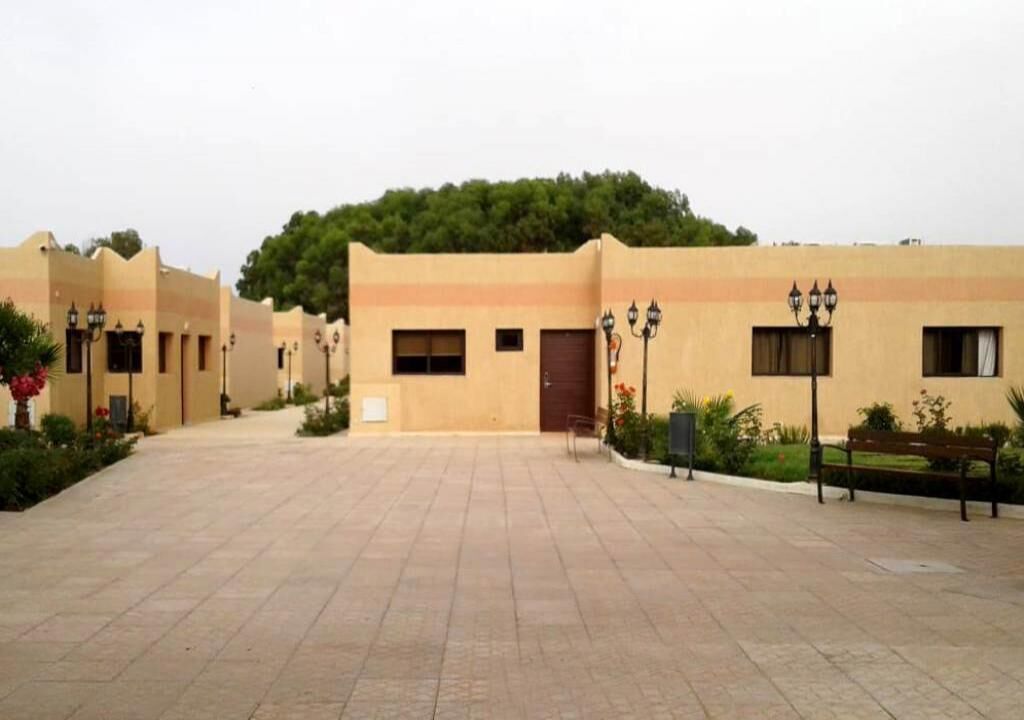 A courtyard with a building featuring a flat roof and a small entrance.