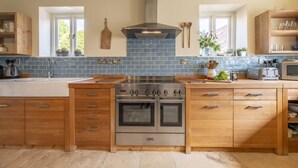 A modern kitchen with wooden cabinets, a stainless steel stove, and a blue-tiled backsplash. - The Old Dairy, Great Bircham, Norfolk (Bircham)