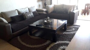 A living room with a dark brown sofa, a glass coffee table, and a patterned rug. - Residence Marrakech Prestigia Opal 2999 (Marrakech)