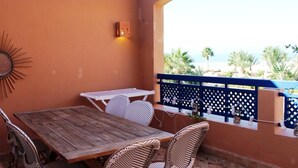 Eine Außenpatio mit Holztisch und Korbstühlen, einem dekorativen Wandbild und Blick auf den Strand.