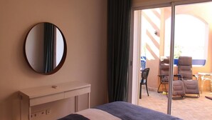 Ein Hotelzimmer mit Bett, Schreibtisch, Stuhl und einem Balkon mit Sitzgelegenheiten.