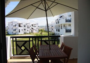 Un balcon avec une table et des chaises, un parasol et une vue sur des immeubles d’habitation blancs.