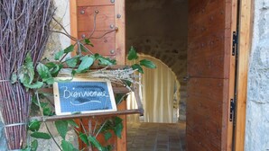 A rustic wooden door with a welcome sign, a tiled floor, and a stone wall. - La Chapelle Saint Gervais (Sospel)