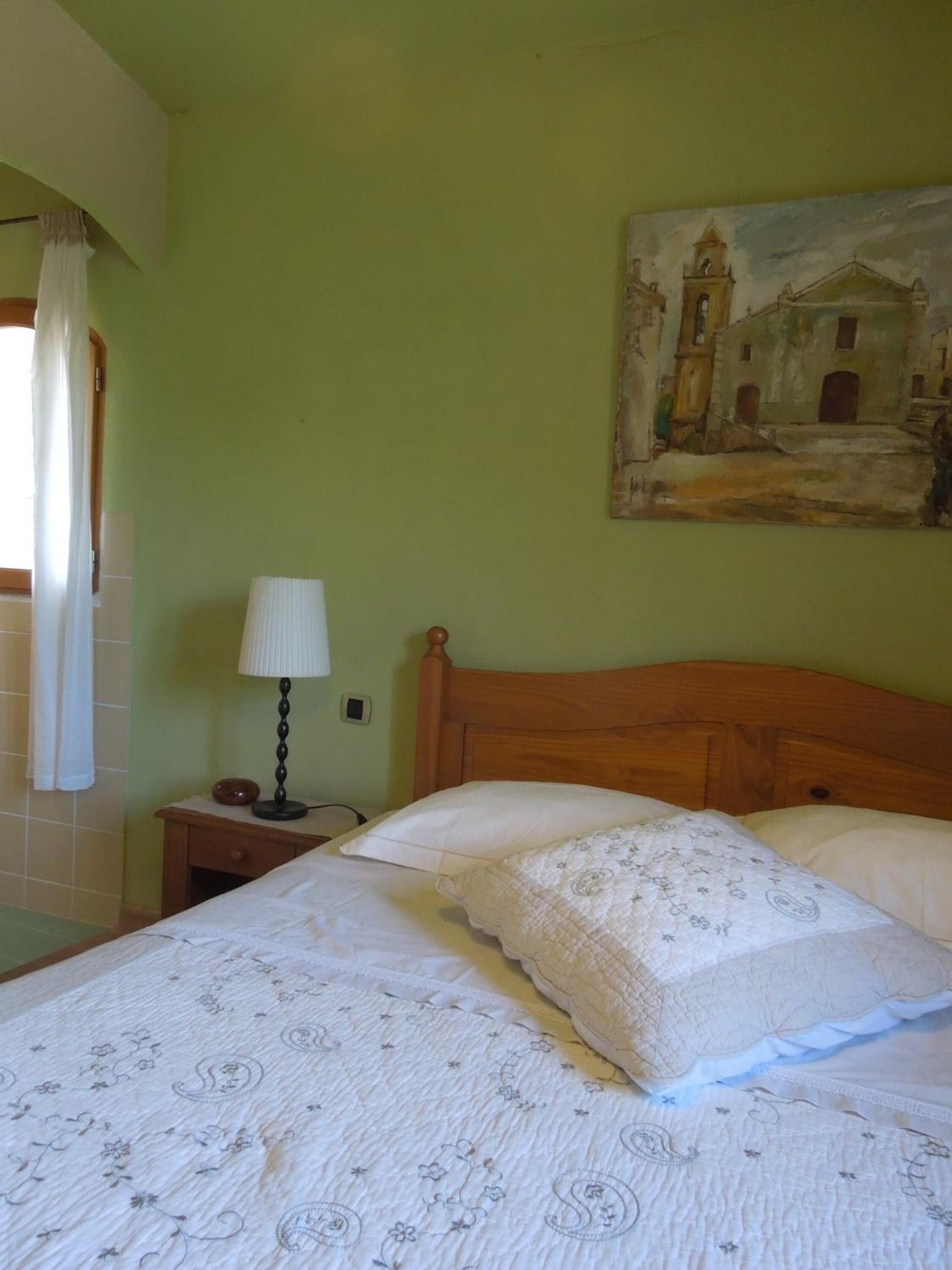 Una camera da letto con un letto, un comodino con una lampada, un quadro appeso al muro e una finestra con tende.