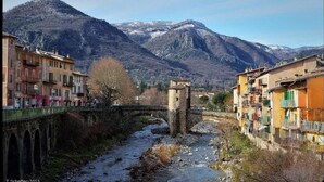 A river flowing through a town with a stone bridge and buildings on either side. - La Chapelle Saint Gervais (Sospel)