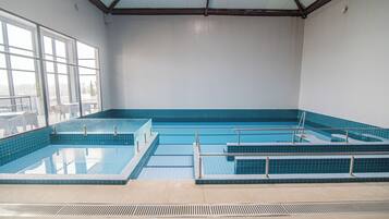 An indoor swimming pool with multiple lanes, safety railings, and a clear view of the outside through large windows.