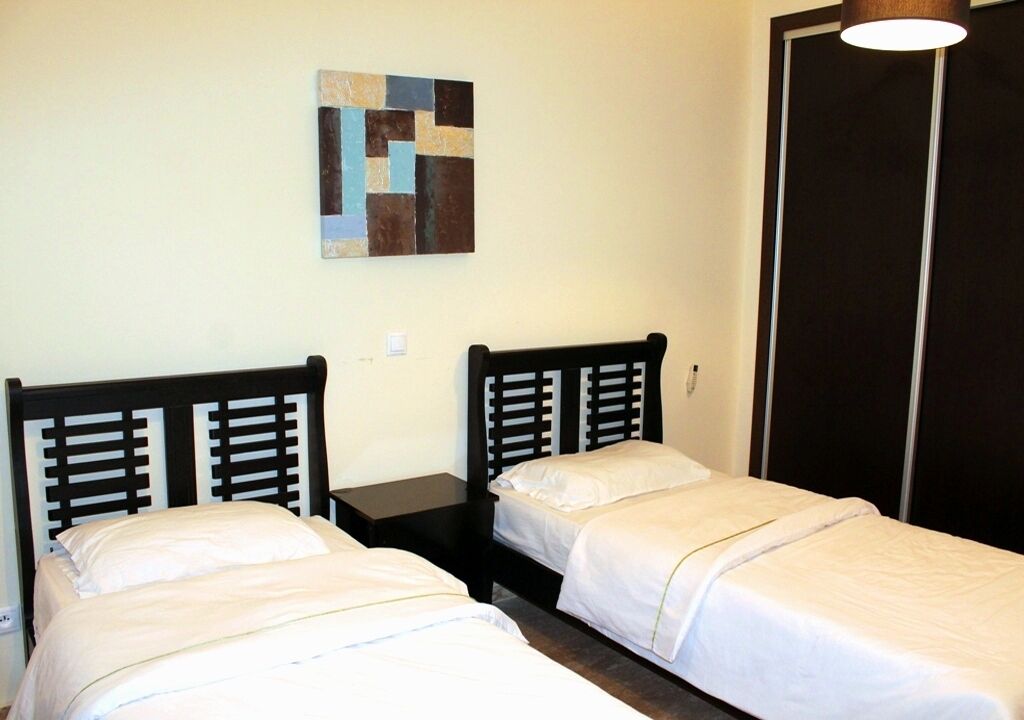 A room with two single beds, a small table, a wall-mounted artwork, and a wardrobe.