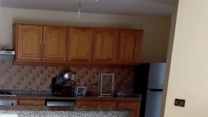 Una cocina con armarios de madera, encimera de granito, lámpara de araña y microondas.