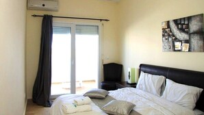 A hotel room with a bed, a chair, a painting on the wall, and a window with curtains. - The Greens Residence 3613 (SAIDIA)