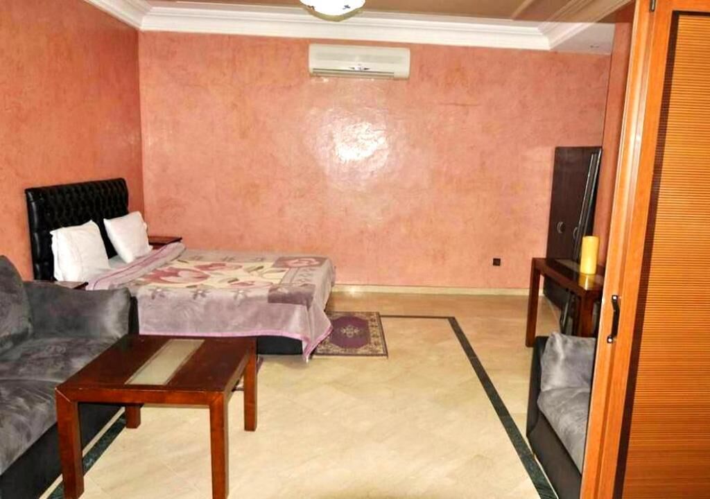 A room with a bed, a sofa, a wooden table, a television, and a door.