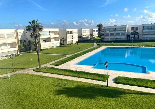 A modern hotel with a swimming pool, green lawns, and palm trees.