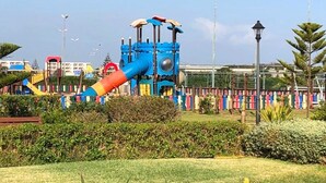 Une aire de jeux avec un toboggan bleu et rouge, entourée de verdure et d’une clôture.