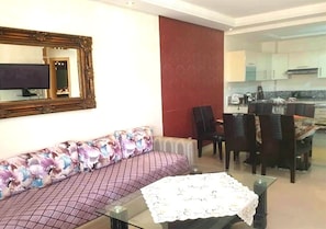 A living room with a sofa, a glass coffee table, and a dining area with chairs and a table.