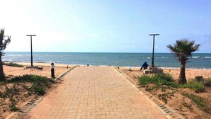 Un chemin pavé mène à une plage bordée de palmiers et illuminée de lampadaires.