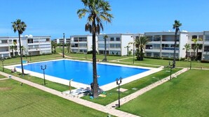 Une piscine entourée de pelouse bien entretenue et de palmiers, avec un bâtiment en arrière-plan.