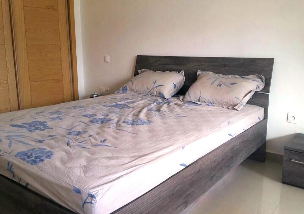 Un dormitorio con una cama, dos almohadas, cabecera de madera, mesita de noche y armario.