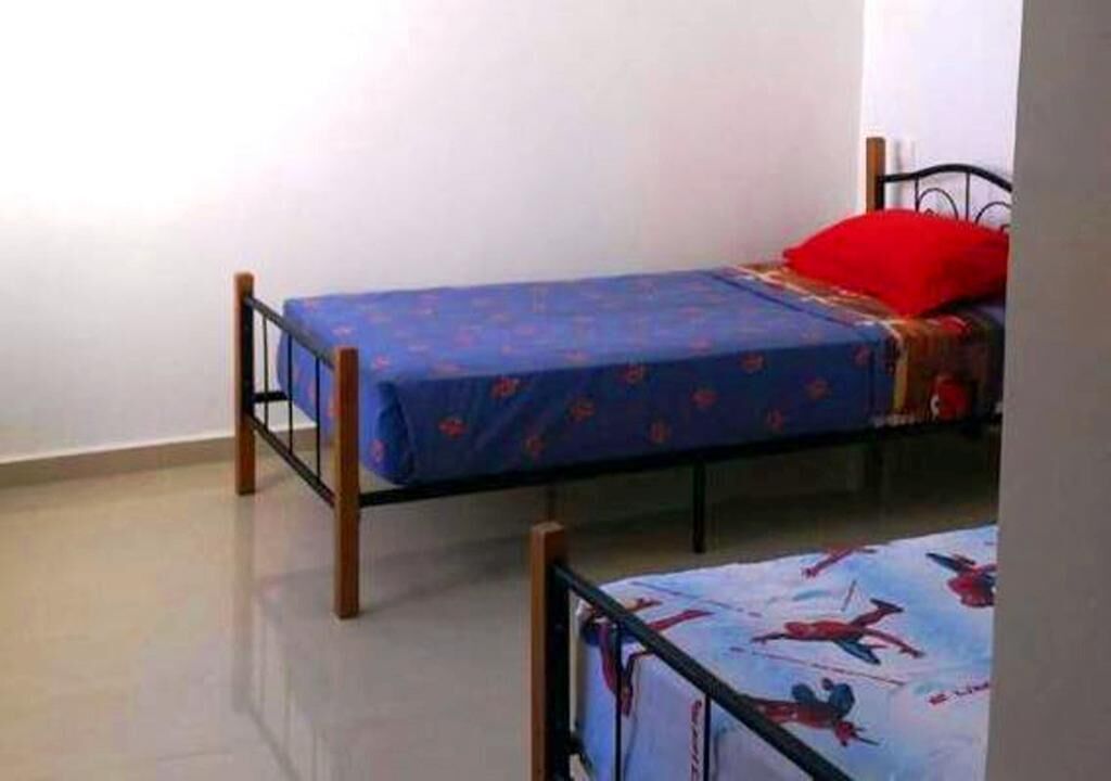 Quarto pequeno com duas camas de solteiro, cada uma com colcha azul e travesseiro vermelho.