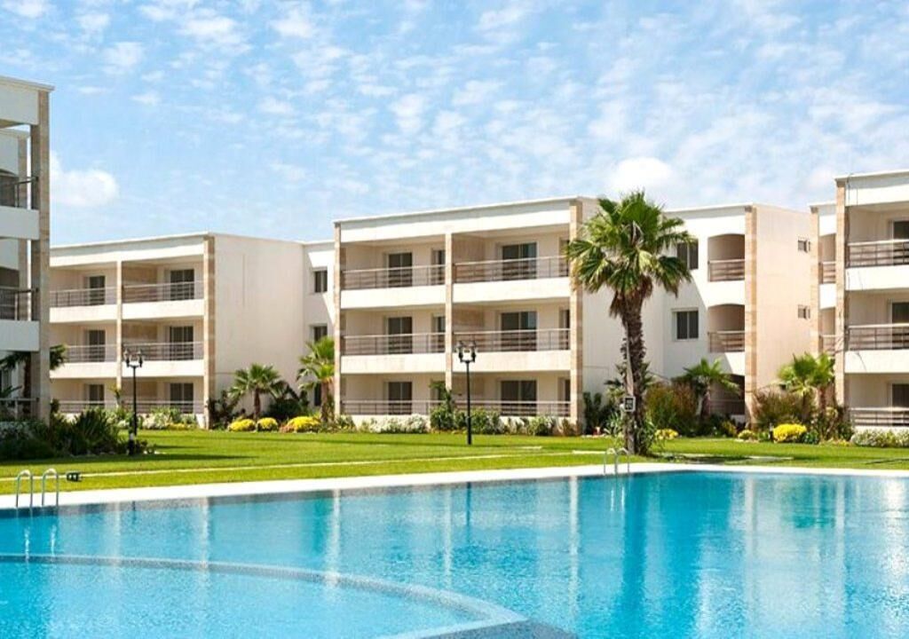 Ein modernes Hotel mit Schwimmbad, mehreren Balkonen und üppiger Bepflanzung.